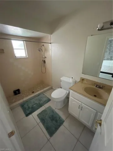 Bathroom with toilet, tile patterned floors, a tile shower, and vanity