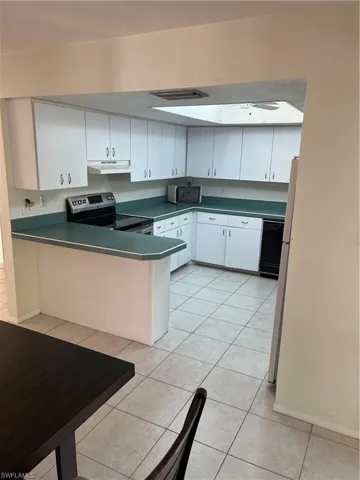 Kitchen featuring light tile patterned flooring, a peninsula, stove, exhaust hood, and dark countertops
