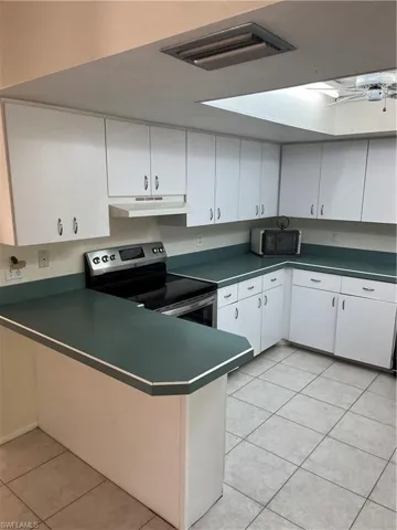 Kitchen with dark countertops, electric range oven, white cabinetry, light tile patterned flooring, and extractor fan