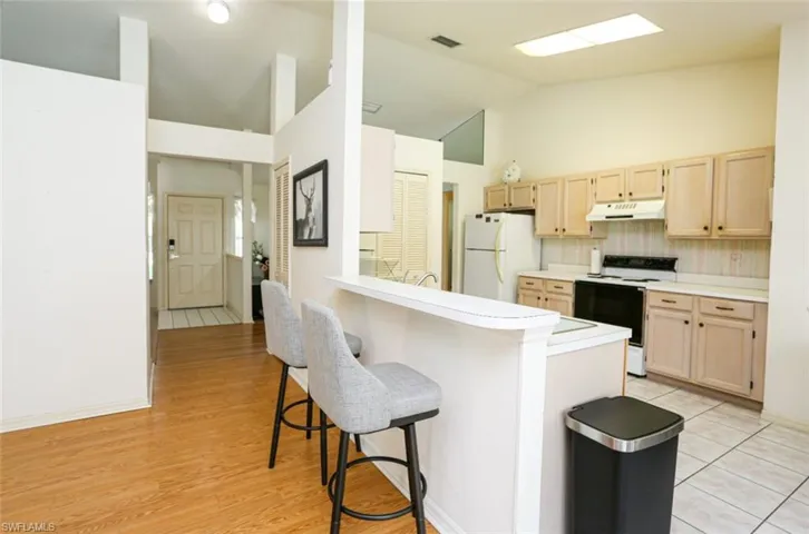 Kitchen with a breakfast bar, white appliances, backsplash, and light brown cabinetry