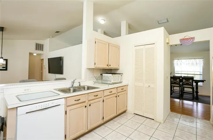 Kitchen with sink, vaulted ceiling, white appliances, light brown cabinetry, and light tile patterned flooring