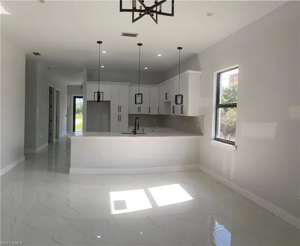 Kitchen featuring a peninsula, healthy amount of natural light, light marble finish flooring, white cabinetry, and recessed lighting