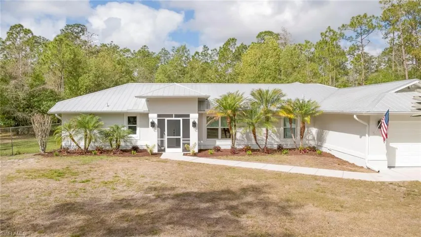 View of front of home with a garage, a metal roof, a sunroom, and a front lawn