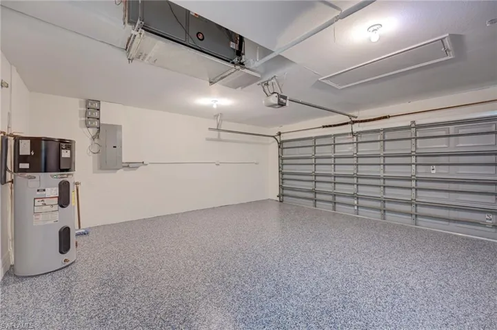 Garage with hybrid water heater, electric panel, and a garage door opener