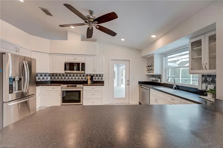 Kitchen with stainless steel appliances, dark countertops, backsplash, white cabinetry, and recessed lighting