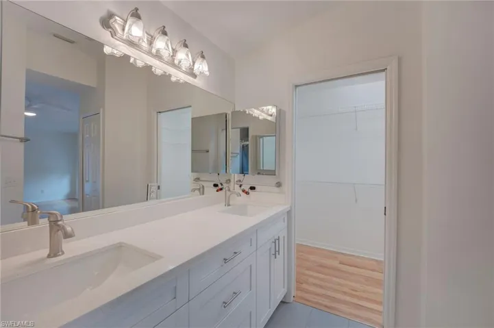 Full bath with double vanity, a spacious closet, and light wood-type flooring