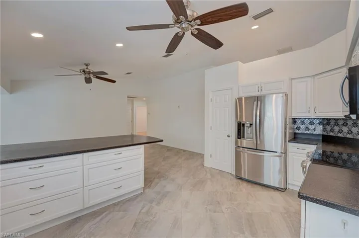 Kitchen with stainless steel appliances, ceiling fan, white cabinets, recessed lighting, and dark stone countertops
