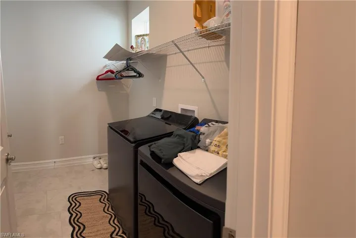 Dedicated laundry area featuring modern appliances, wire shelving, and light-toned flooring