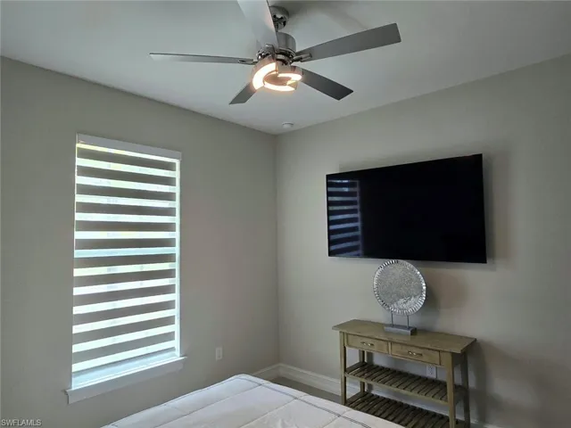 Wall-mounted television with a console table, ceiling fan with integrated lighting, and window with banded shades