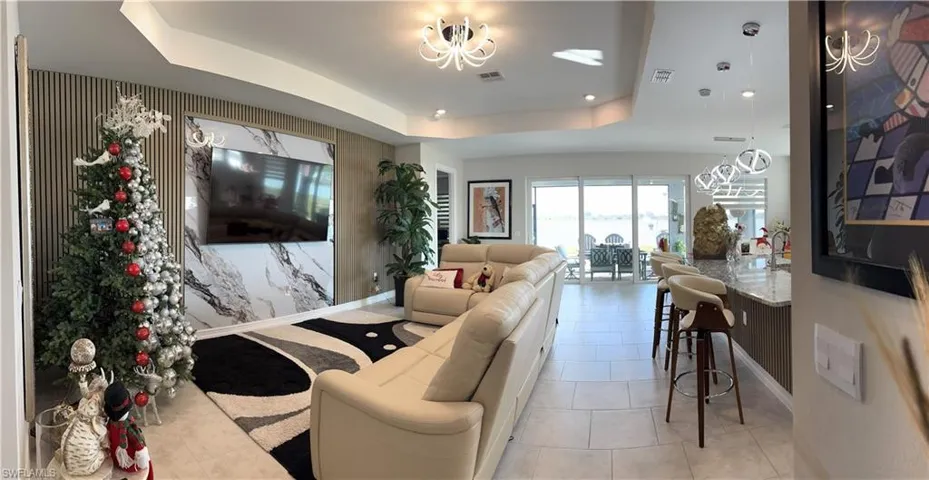 Open-concept living space with large sliding glass doors, a kitchen island with seating, recessed lighting, and a feature wall with a television insert
