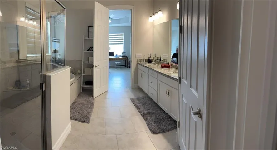 Spacious bathroom featuring a dual vanity with light-toned countertops, a glass-enclosed shower, a separate bathtub, and tile flooring