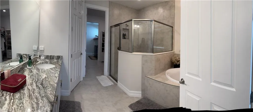 Bathroom featuring a dual vanity with a patterned countertop, a built-in soaking tub, and a glass-enclosed shower