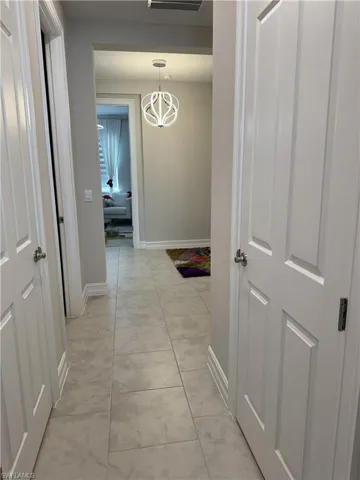 Hallway featuring light-toned tile flooring, white paneled doors, and a contemporary spherical pendant light