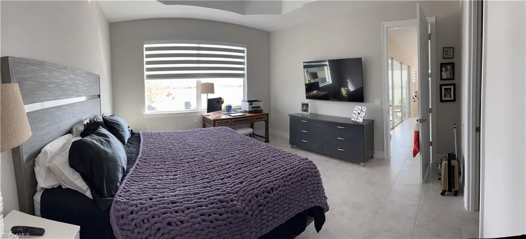 Spacious room featuring neutral-toned walls, tile flooring, a large window with horizontal blinds, and a tray ceiling