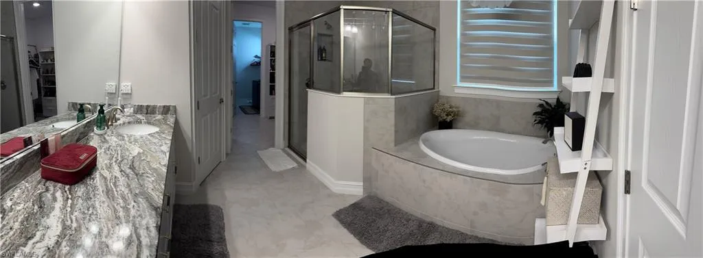 Spacious bathroom featuring a large soaking tub, glass-enclosed shower, dual vanity with undermount sinks, and a stone-finish countertop