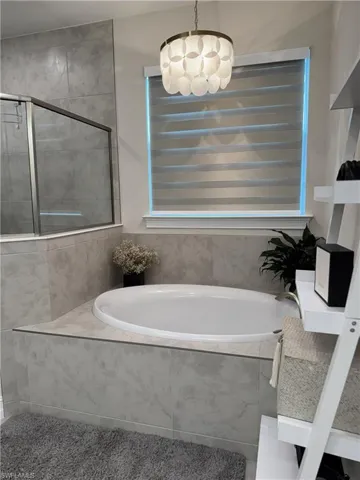 Built-in soaking tub with gray tile surround, contemporary chandelier lighting, and a frosted window with blinds