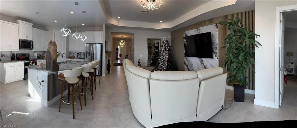 Open-concept living area featuring a kitchen island with pendant lighting, white cabinetry, stainless steel appliances, and tile flooring