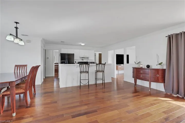 Kitchen featuring white cabinets, ornamental molding, black fridge with ice dispenser, dark wood-style flooring, and light countertops