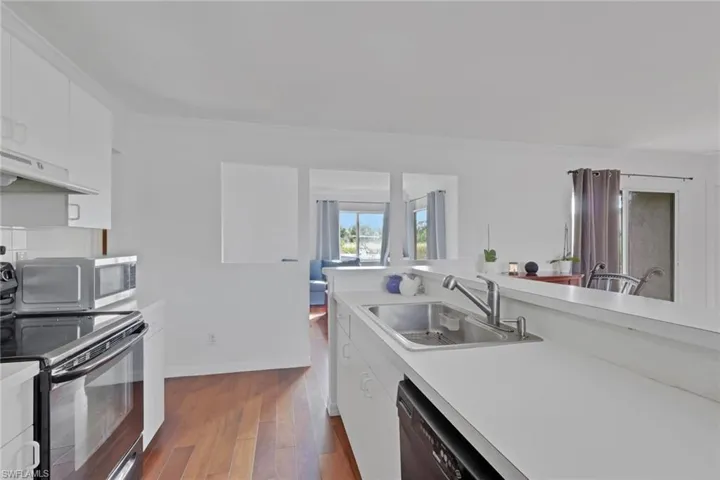 Kitchen featuring white cabinetry, black appliances, light countertops, dark wood finished floors, and crown molding