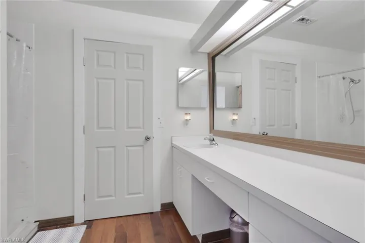 Full bath with a stall shower, vanity, and dark wood-type flooring
