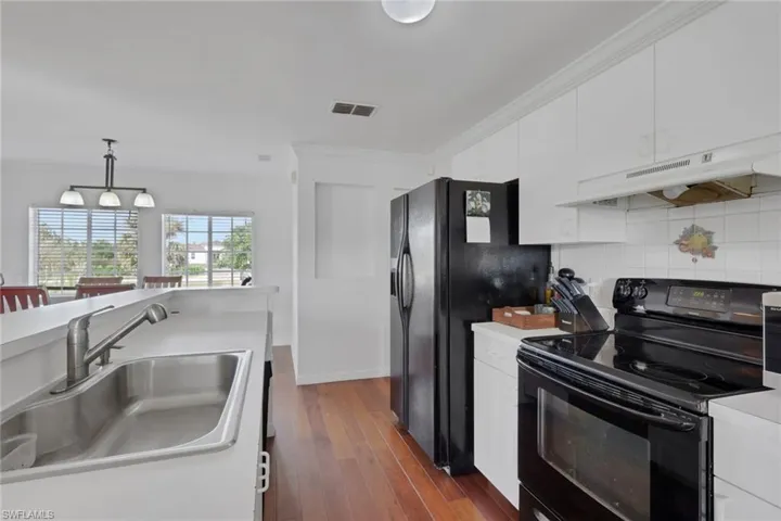 Kitchen featuring black appliances, light countertops, crown molding, white cabinets, and under cabinet range hood