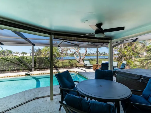 View of pool featuring a patio, a water view, glass enclosure, and ceiling fan
