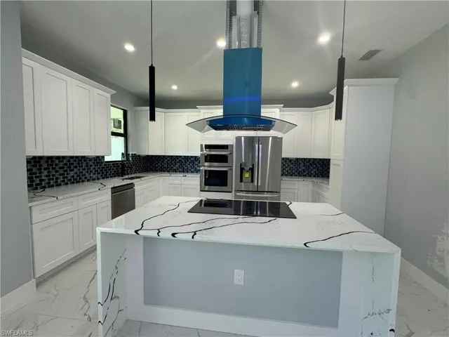 Kitchen with with stainless steel appliances finishes, island induction stove hood, pendant lighting, light stone countertops, and a center island