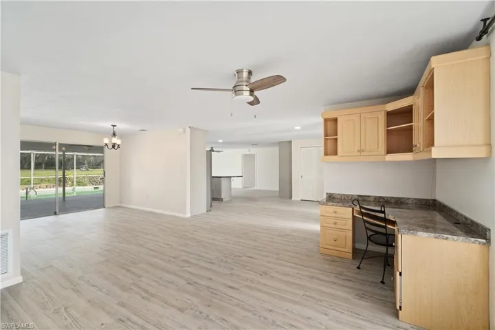 Unfurnished office featuring built in desk, light wood-style floors, ceiling fan, baseboards, and a chandelier