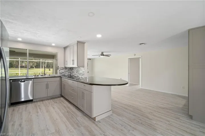 Kitchen with appliances with stainless steel finishes, gray cabinets, a peninsula, light wood-style flooring, and recessed lighting