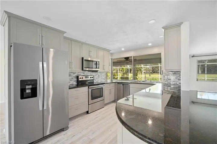 Kitchen with stainless steel appliances, gray cabinets, decorative backsplash, a sink, and dark stone countertops