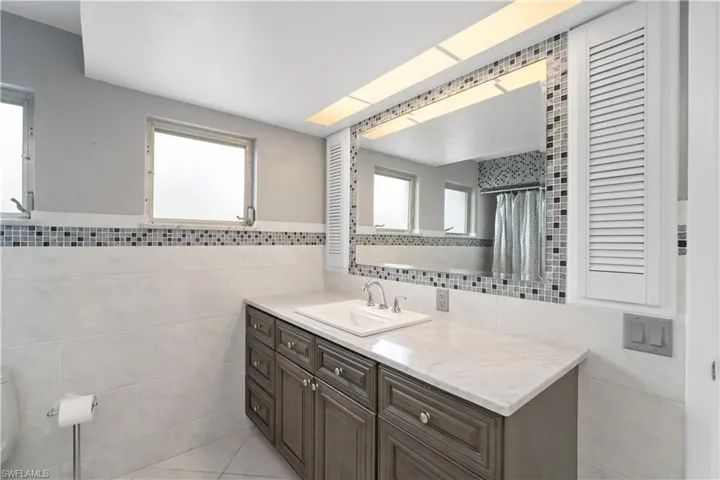Full bathroom featuring tile walls, vanity, plenty of natural light, tile patterned floors, and a wainscoted wall