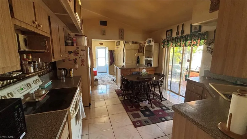 Kitchen with white range with electric cooktop, dark countertops, light tile patterned floors, vaulted ceiling, and black microwave