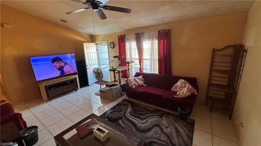 Living room with light tile patterned flooring, vaulted ceiling, a ceiling fan, and a textured ceiling