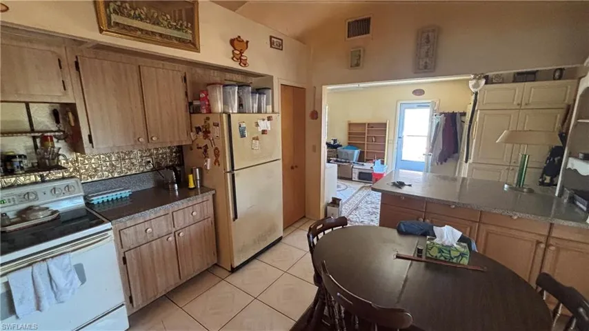 Kitchen featuring white appliances, light tile patterned floors, dark stone counters, and decorative backsplash