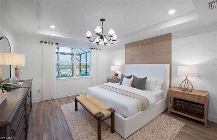 Bedroom with a raised ceiling, an inviting chandelier, and wood-type flooring