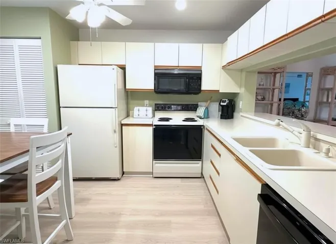 Kitchen with black appliances, light countertops, light wood-type flooring, ceiling fan, and white cabinets