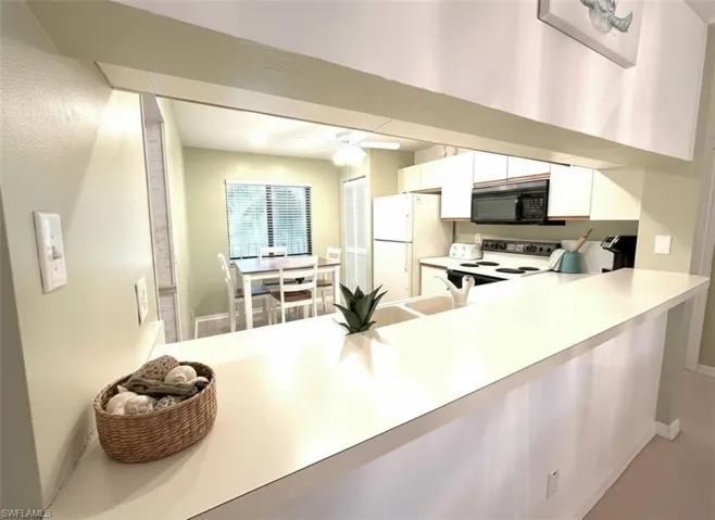 Kitchen with light countertops, electric range oven, white cabinets, a peninsula, and black microwave