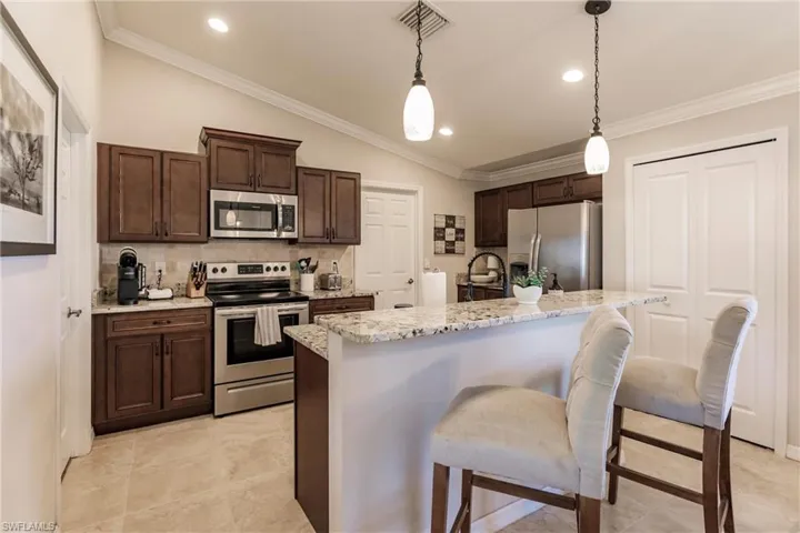 Kitchen featuring a center island with sink, light tile flooring, decorative light fixtures, ornamental molding, and appliances with stainless steel finishes