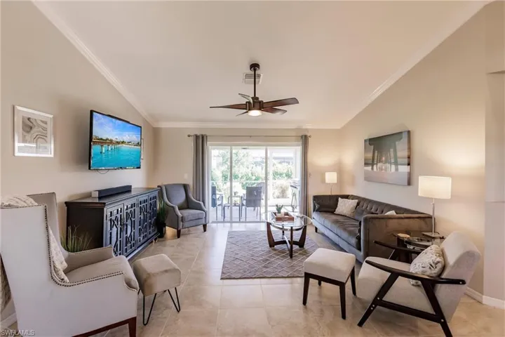 Living room with lofted ceiling, ornamental molding, ceiling fan, and light tile floors