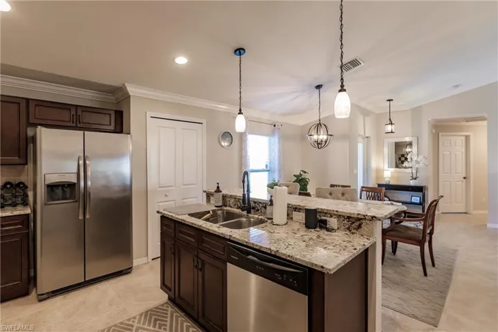 Kitchen with decorative light fixtures, light tile floors, sink, a kitchen island with sink, and appliances with stainless steel finishes