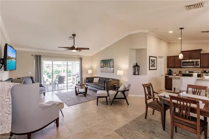 Tiled living room with vaulted ceiling, ornamental molding, and ceiling fan