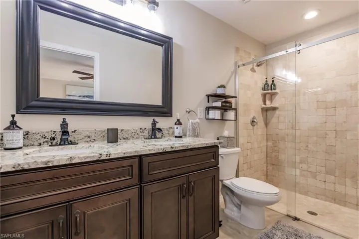 Bathroom with double sink vanity, a shower with shower door, ceiling fan, and toilet