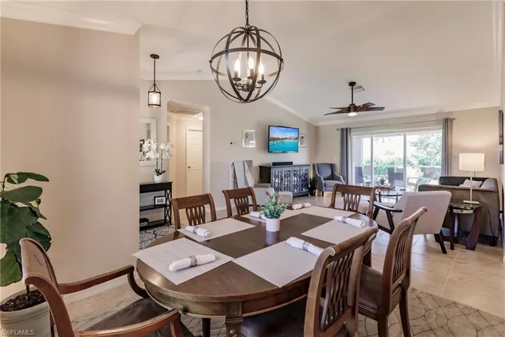 Tiled dining space featuring crown molding, vaulted ceiling, and ceiling fan with notable chandelier