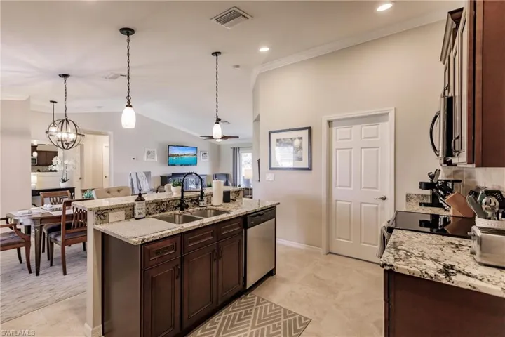 Kitchen featuring decorative light fixtures, light stone counters, stainless steel appliances, sink, and light tile floors