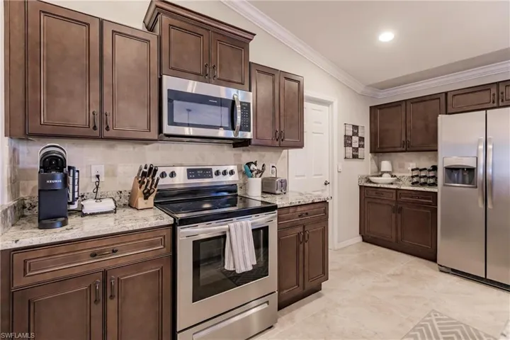 Kitchen with light stone countertops, backsplash, light tile floors, lofted ceiling, and appliances with stainless steel finishes