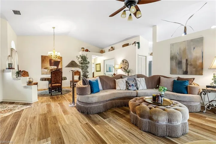 Living room featuring light wood-type flooring, vaulted ceiling, and ceiling fan with notable chandelier