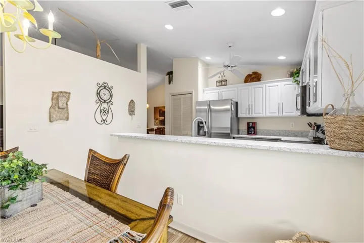 Kitchen with ceiling fan, vaulted ceiling, light stone countertops, white cabinets, and stainless steel fridge