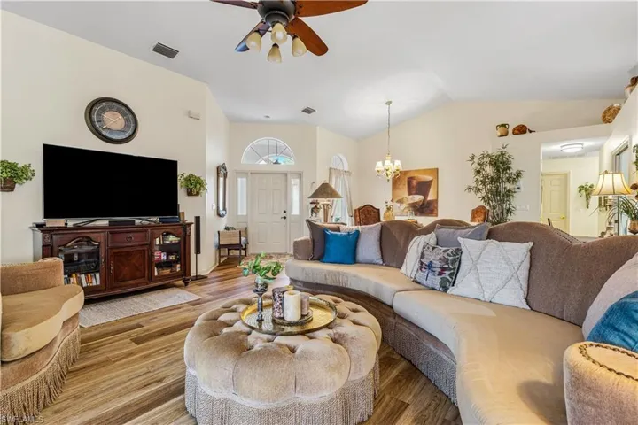 Living room featuring ceiling fan with notable chandelier, lofted ceiling, and light wood-type flooring
