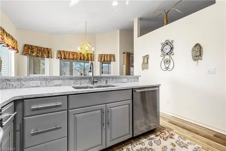 Kitchen featuring gray cabinetry, a notable chandelier, light wood-type flooring, stainless steel dishwasher, and sink