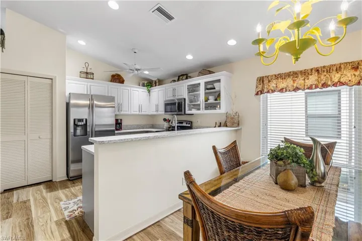 Kitchen with vaulted ceiling, light hardwood / wood-style floors, hanging light fixtures, stainless steel appliances, and white cabinets